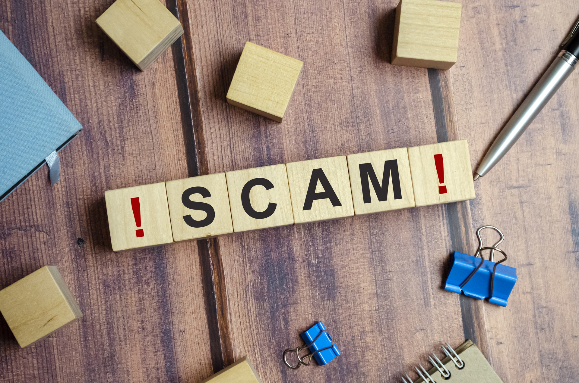 The word SCAM is written on wooden blocks on a wooden background